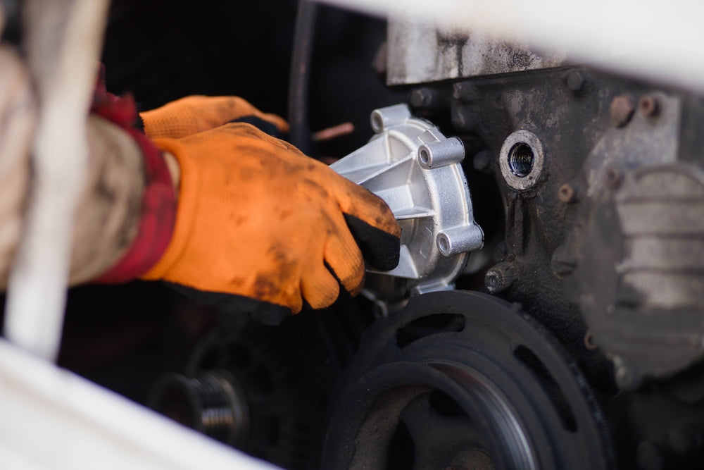 A man wearing orange gloves replaces a gear on an industrial robot