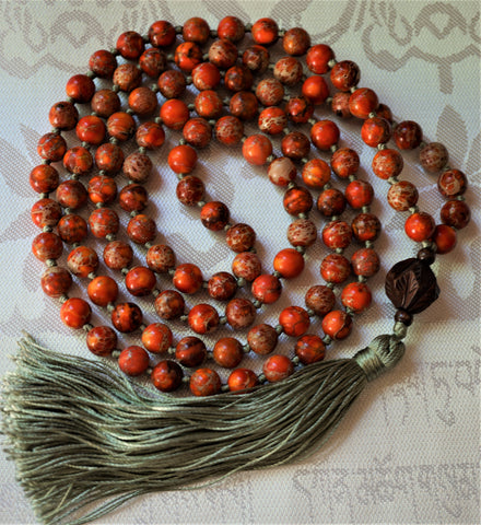 full view of orange jasper mala with silk green tassel and carved wooden guru.