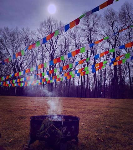Bright prayer flags hang and flutter over smoldering remains of fire puja