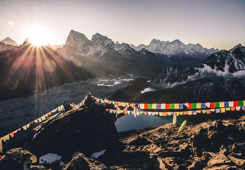View of Himalayan mountain peaks and valleys with prayer flags in the foreground and a setting sun in the background