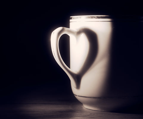 White teacup in shadow. The reflection of the handle creates a heart shaped image