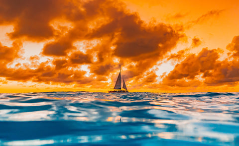 image of a white sailboat on blue water with a bright orange sky and clouds