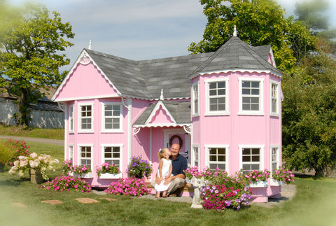Pink playhouse or mini mansion with a dad and his daughter sitting in front of it.
