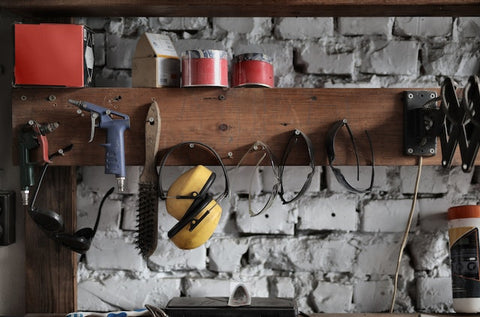 Tools, equipment, and paint hanging on pegs or sitting on shelf that is placed in barn shed.