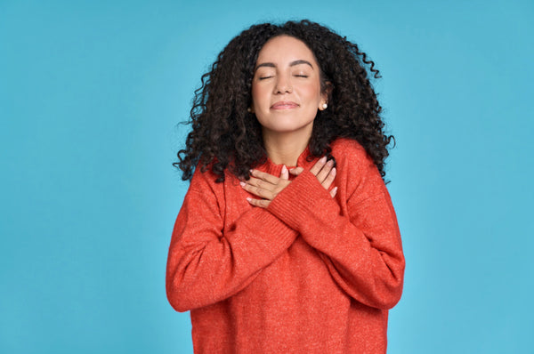 Happy Latin woman holding hands on chest in gratitude