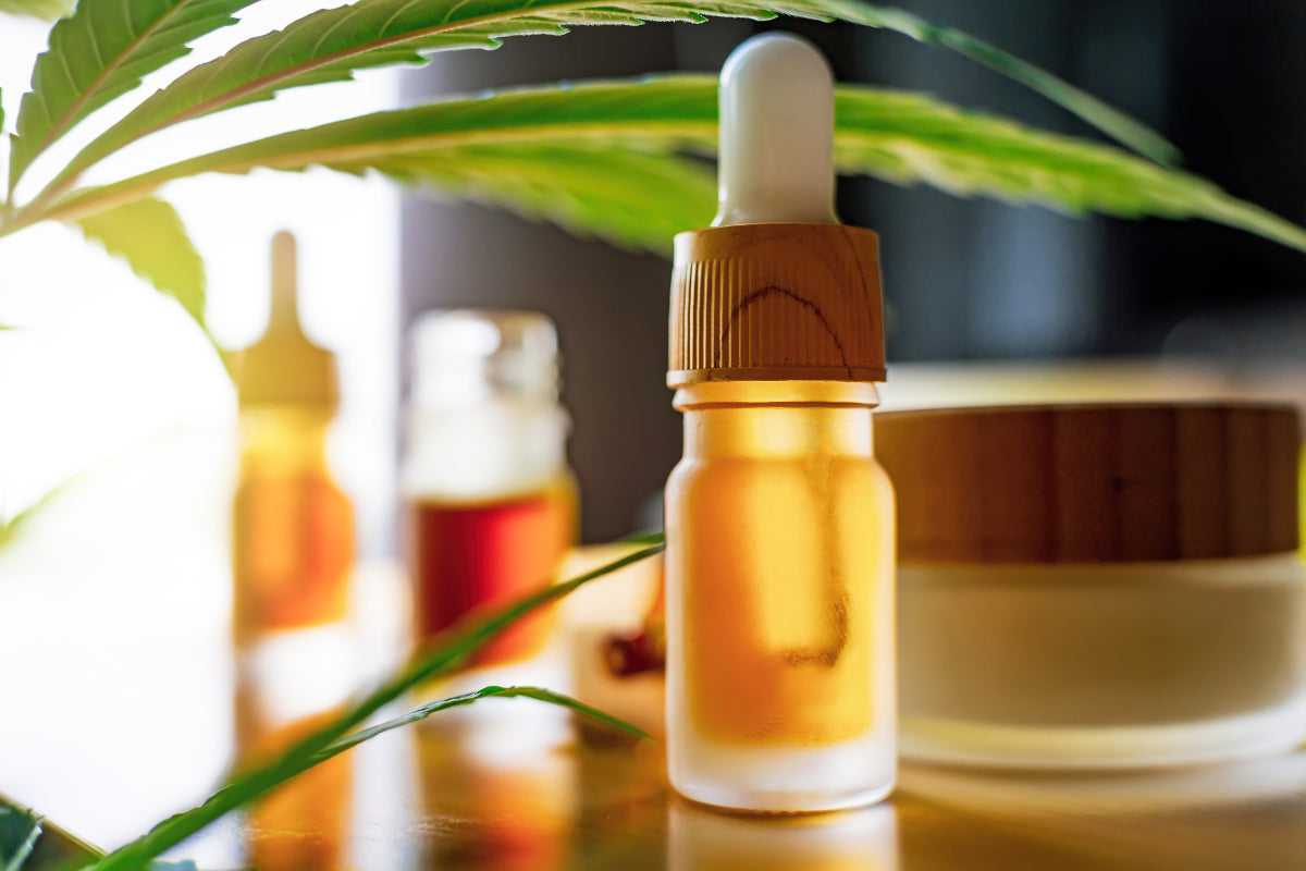 Sueros y crema hidratante de CBD sobre una mesa rodeada de hojas de cáñamo.