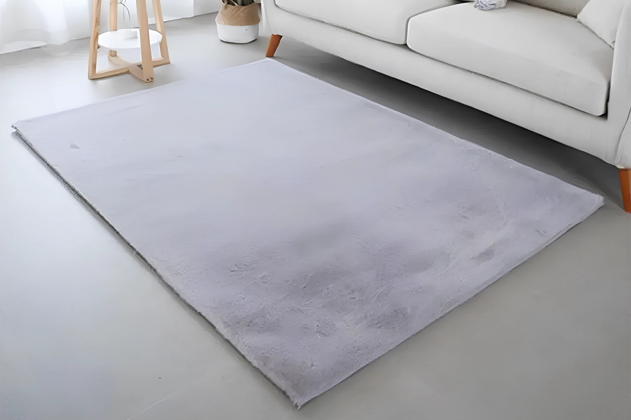 Tapis rectangulaire doux de couleur gris clair placé dans un salon moderne, à côté d’un canapé blanc et d’un petit meuble en bois clair