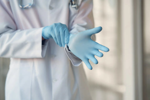 person wearing lab coat putting on blue gloves
