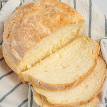 a round loaf of artisan gluten free bread is shown. It is sliced, revealing soft crumb that holds together well.