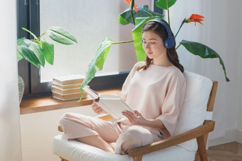 窓辺で読書をしながら音楽を聴く女性