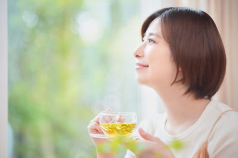 窓辺でハーブティーを飲む女性