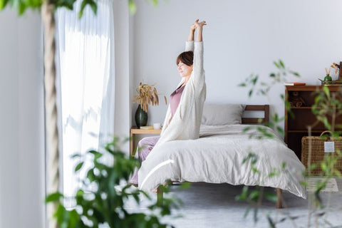 観葉植物のある寝室で伸びをする女性