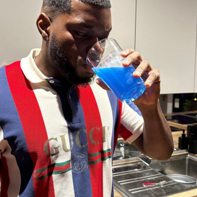 Man drinking blue liquid from a clear glass.