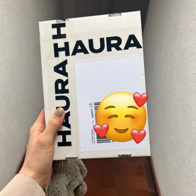 Person holding a parcel with the word 'HAURA' and a smiling emoji with hearts covering the address.