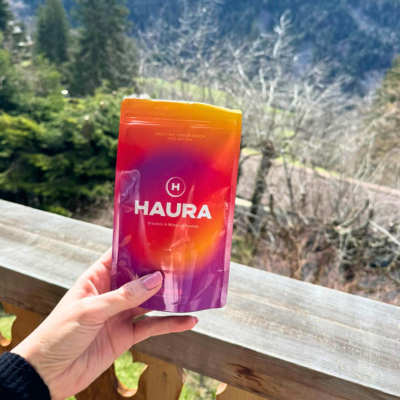 Hand holding a Haura skincare product against a natural, forested background.