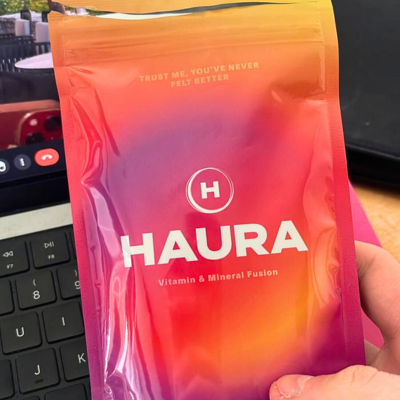 Hand holding a colorful pouch labeled HAURA Vitamin & Mineral Fusion.