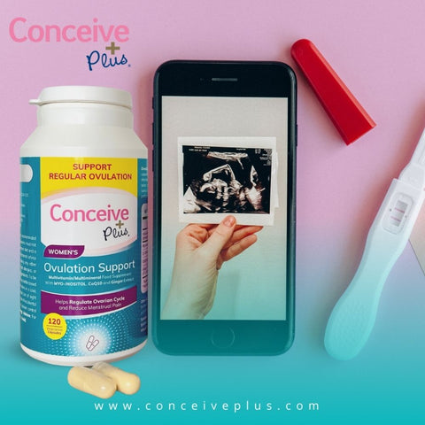 Un teléfono móvil con una imagen de una mano sosteniendo una ecografía de embarazo en la pantalla y una tira de embarazo con resultado positivo a la derecha y una botella de apoyo a la ovulación Conceive Plus en el lado izquierdo