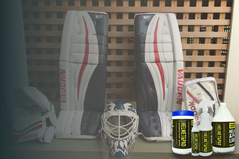 Goalie pads laid out on a clean surface with a person wiping them down using a cloth and disinfectant spray