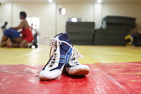 Step-by-step process of cleaning wrestling shoes, illustrating brushing, application of Matguard cleaning solution, and wiping techniques.