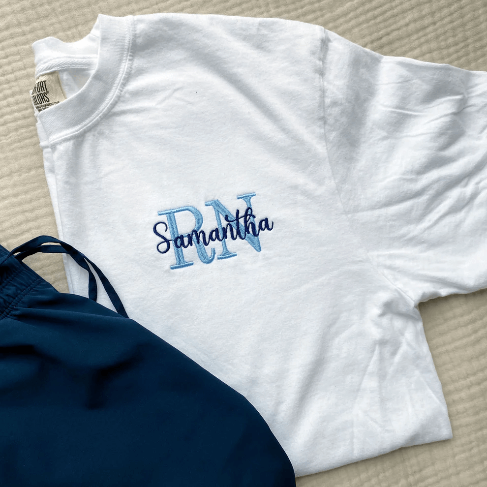 A white nurse t-shirt with blue initials on a tan bedspread