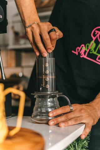 Person applying pressure on an Aeropress coffee maker to extract coffee.