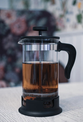French press style coffee pot filled with extracted coffee on a white table.