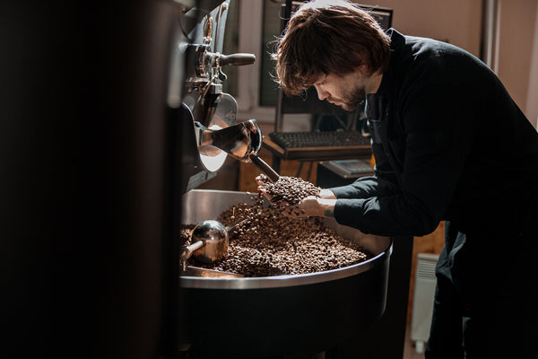 Hombre cogiendo café tostado con las manos del depósito de una tostadora.