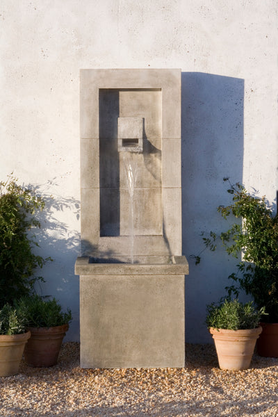 Tall rectangular fountain shown running in front of white wall