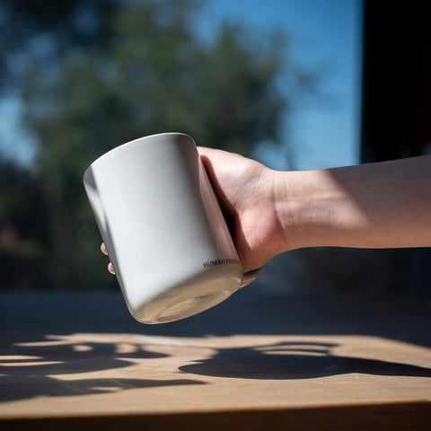 A hand holding the CURVD mug lifted above a table.