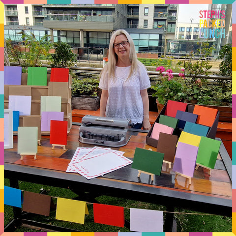 Hayley at her market stall on Steph's Packed Lunch, lots of colourful braille cards on display with a perkins brailler.