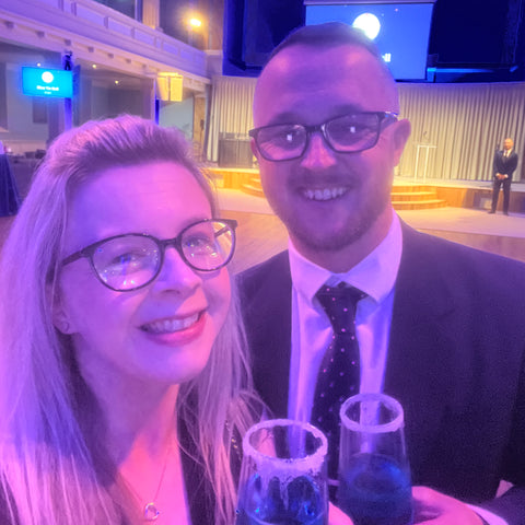 Hayley with her husband Scott at the Blue Tie Ball, both are holding blue coloured drinks and are smiling at the camera