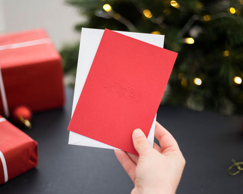 Hands holding a red braille Christmas card with Merry Christmas written in lower case UEB.