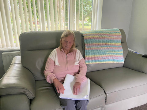 Bridget troy sitting on a sofa, reading a braille book