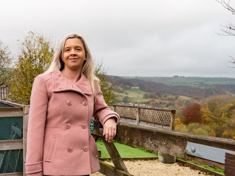 Hayley Kellard wearing a pink winter coat, stood against a fence with gorgeous scenery in the background