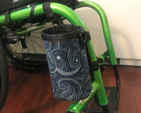A patterned fabric cup holder attached to the green bars of a wheelchair.