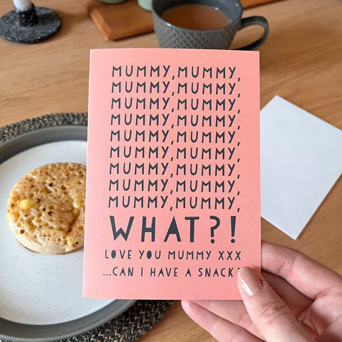 A hand holding a pink card saying mummy multiples times followed by WHAT?! I Love You Mummy, can I have a snack? There is a white envelope in the background.