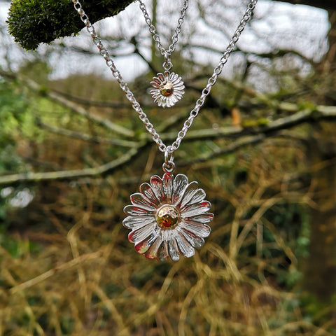 Sterling silver and gold daisy pendants hanging from a tree branch, daisy jewellery handmade in Ireland.