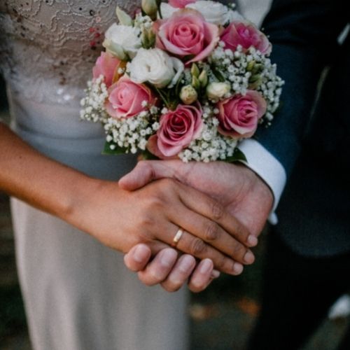 A bride and groom hold hands while the bride shows her bouquet in a close up