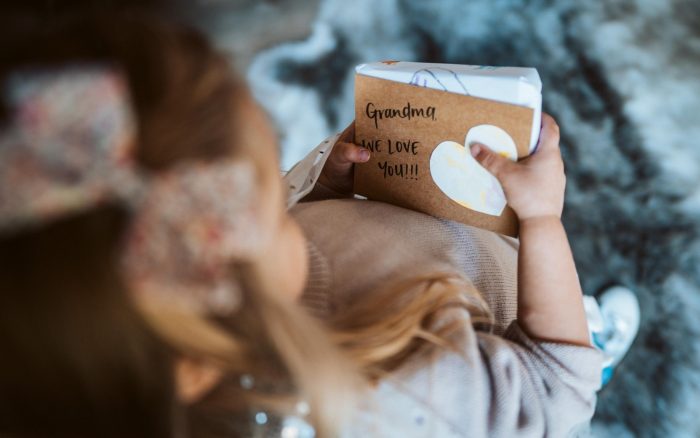 Kleines Mädchen auf dem Schoß einer Frau mit einem Buch, auf dem „Oma“ steht