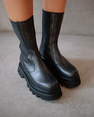 model wearing mid calf black leather boots with elastic sides and chunky soles