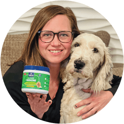 A woman holding a container of dog supplement while hugging a fluffy dog.