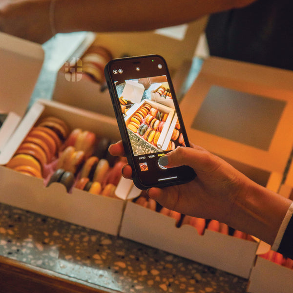 a hand holding mobile phone taking pictures of macarons by pretty sweet