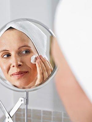 A woman looking in a mirror and spreading a cream on her face