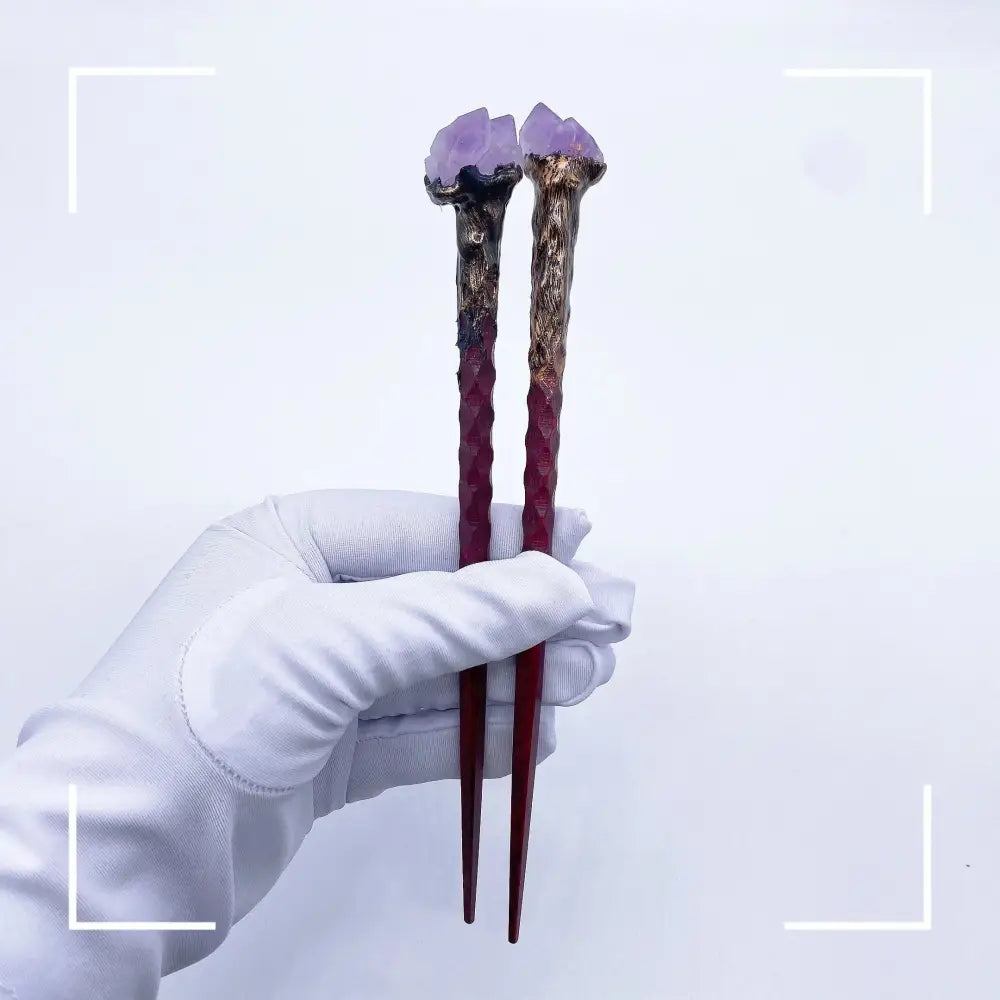 Two decorative chopsticks with natural amethyst flower crystal magic at tips held by gloved hand