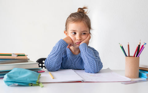 little girl at desk grumpy and distracted from doing homework