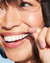 A brunette model with her mouthh slightly open and smiling, looking away, using a piece of Reach POP Mint Dental Floss