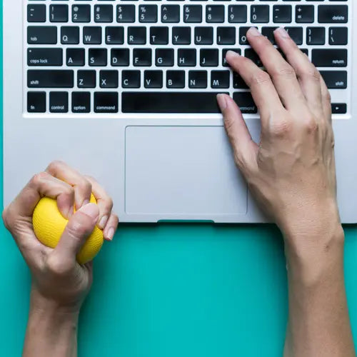 deux mains d'homme, une sur un clavier d'ordinateur et l'autre tenant une balle anti stress