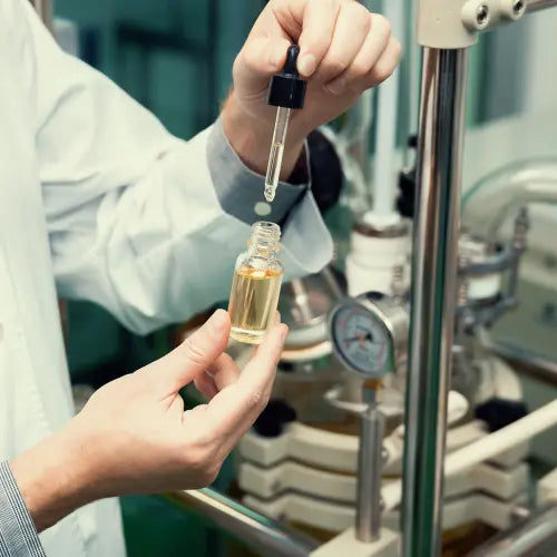 man holding a vial and a pipette filled with oil in front of an extractor