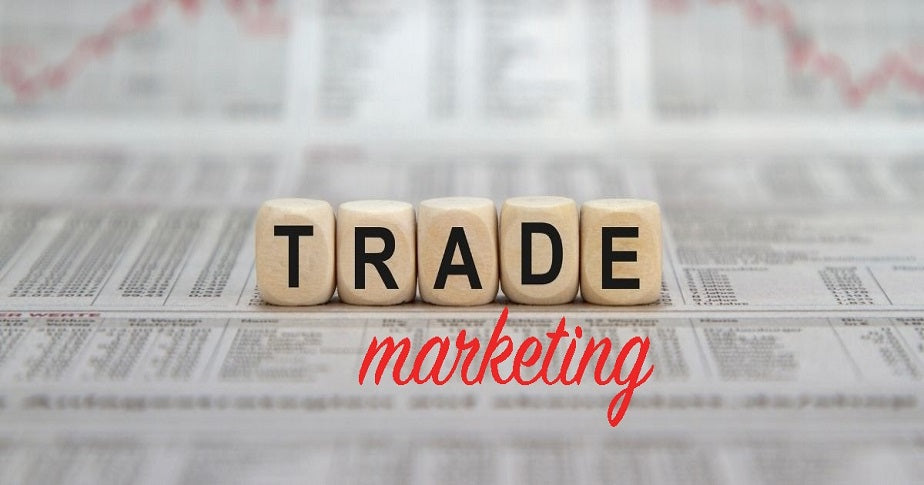 blocos de letras escrito trade com palavra logo abaixo escrito marketing formando o termo trade marketing acima de folhas de dados