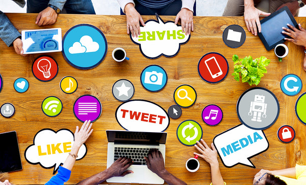 mesa de reunião com várias pessoas em seus laptops e tablets com balões indicando ações de social selling, como like e share e outros símbolos de redes sociais e outras ações